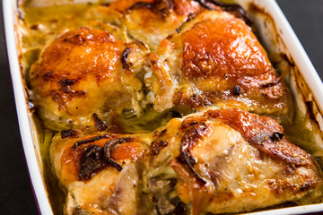 Baked chicken thighs with onions in ceramic form on a stone table, copy space.