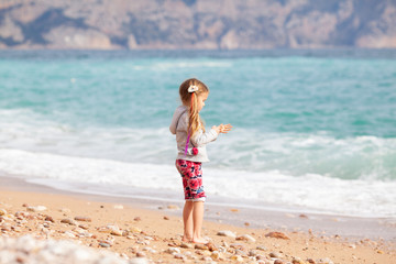 Happy pretty girl walks along the sea coast against the background of the sea, from behind a beautiful landscape