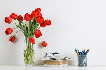 Red tulips in a vase, books and school supplies on a white background. The concept of a postcard for teacher's day. Copy space.