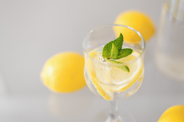Glass of cocktail with sparkling mineral water, lemon and mint on glass table. Green and yellow colour. Citrus lemonade