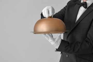 Handsome male waiter with tray and cloche on grey background
