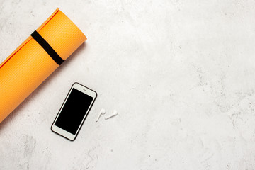 Yoga and fitness mat and phone on a light stone background. Fitness or yoga online concept. Banner. Copy space. Flat lay, top view