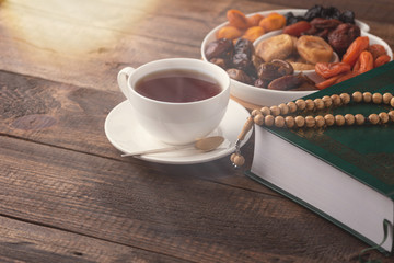Iftar, Ramadan, Koran, Cup of tea, plate of dried fruit on brown wooden background
