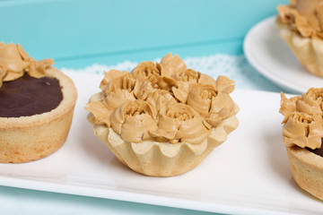 Chocolate ganache tartlets and cakes. Decorated with oil cream flowers. The cream has a caramel color. In a tray of turquoise color.