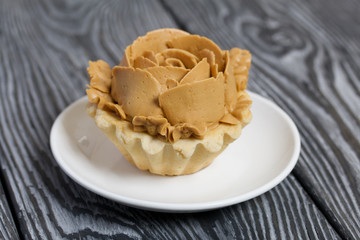 Half a cake decorated with butter cream flowers. The cream has a caramel color. On brushed pine boards painted black.