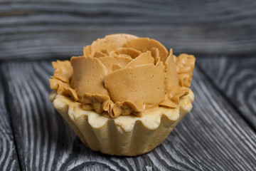 Half a cake decorated with butter cream flowers. The cream has a caramel color. On brushed pine boards painted black.