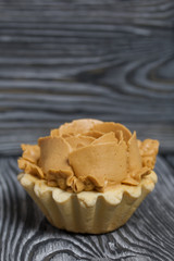 Half a cake decorated with butter cream flowers. The cream has a caramel color. On brushed pine boards painted black.