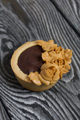 Tartlets with chocolate ganache. Decorated with oil cream flowers. The cream has a caramel color. On brushed pine boards painted black.
