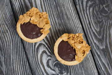 Tartlets with chocolate ganache. Decorated with oil cream flowers. The cream has a caramel color. On brushed pine boards painted black.