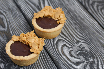 Tartlets with chocolate ganache. Decorated with oil cream flowers. The cream has a caramel color. On brushed pine boards painted black.