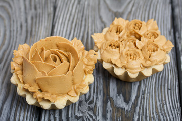Half a cake decorated with butter cream flowers. The cream has a caramel color. On brushed pine boards painted black.