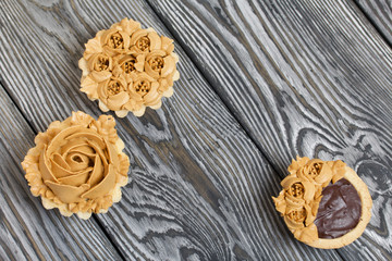 Fototapeta na wymiar Chocolate ganache tartlets and cakes. Decorated with oil cream flowers. The cream has a caramel color. On brushed pine boards painted black.