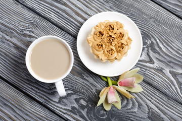 Cupcake and a cup of coffee with milk. Nearby are orchid flowers. Cake decorated with flowers made of butter cream. The cream has a caramel color. On brushed pine boards painted black.