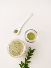  matcha tea in a clear glass with flowers and spoon on yelow background. Trendy vegan drink.