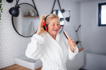 Portrait of senior woman with headphones and bathrobe indoors at home.