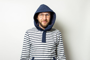 Fototapeta na wymiar Portrait of a Bald Young man with a beard in glasses, a sweater with a hood on an isolated light background. Emotional face. Man in the hood