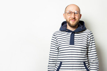 Obraz premium Portrait of a Bald Young man with a beard in glasses, a sweater with a hood, smiling on an isolated light background. Emotional face