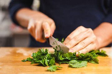 Woman cutting fresh organic parsley and mint on chopping board, making healthy low calories salad.