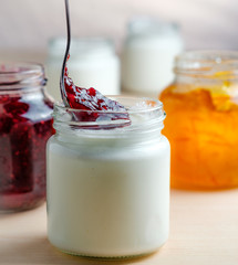 Homemade yogurt with red berries marmalade spoon eating from a glass jar on a white wooden table. Healthy dairy probiotic breakfast.