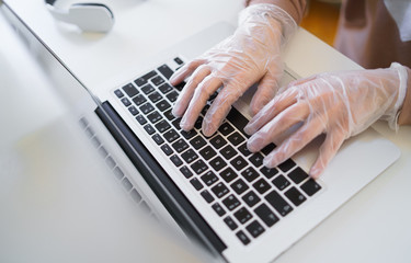 Unrecognizable woman with gloves at the table, using laptop in quarantine.