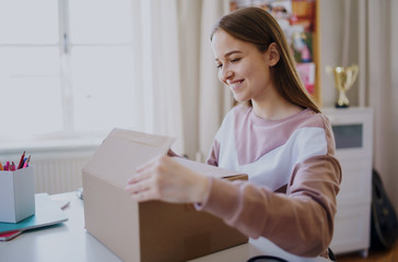 Young female student at the table, opening parcel box.