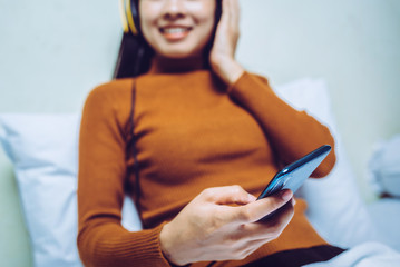 Happy asian girl with hehadphones listening to music or watching tv movie series in mobile on the bed at home.