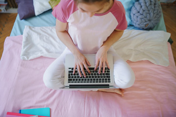 Top view of young girl with laptop on bed, working during quarantine.