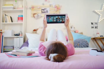 Young girl with tablet on bed, relaxing during quarantine. Copy space.