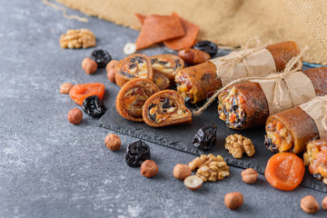 fruit rolls with nuts, dried fruits, honey on gray background, vegetarian snack, healthy bar concept