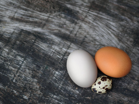 Characteristic of three type eggs: chicken egg, duck egg, and quail egg on wooden background.
