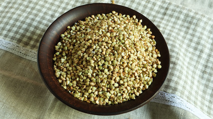 Raw green buckwheat in a brown clay plate on a brown background. Vegan organic food concept. The concept of diet, weight loss, healthy and proper nutrition. Copy space for text. Top view, flat lay.