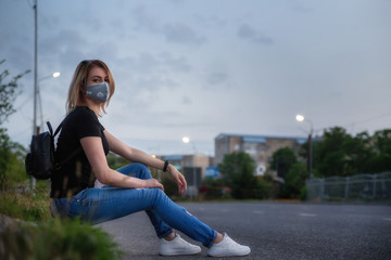Fototapeta premium Girls in medical mask outdoors in an empty city. Sits on the side of the road. Health and prevention of viral epidemics, coronavirus, COVID-19, epidemic, infectious diseases, concept of quarantine