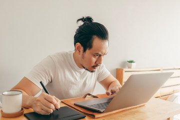 Serious Asian man is working with laptop in his apartment bedroom in concept of Work From Home and Work at Home.