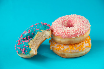 three donuts with white-yellow-pink-blue glaze, on a blue background, sweet dessert festive