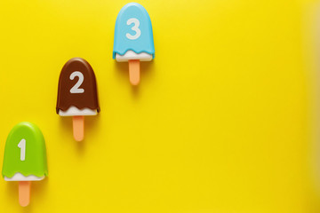 Colorful and various plastic toys ice cream with numbers for babies on a yellow background. Layout. Empty space for the text. Minimalism