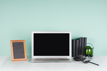 Fresh workplace for education, work with blank notebook screen, black stationery, books, candlestick, photo frame in green mint menthe interior on white wood table.