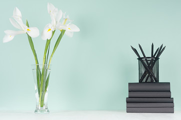 Minimalistic style of home workplace with black stationery, books,  fresh white spring flowers on green mint menthe wall and white wood board.