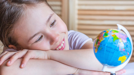 Child girl is smiling and looking at the globe, dreaming about traveling around the world.