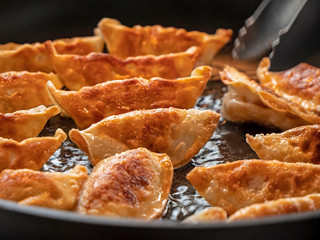Close up of Japanese dumplings. The Gyoza dumplings cook in a pan of hot oil and are turned over to see the golden brown outer side.