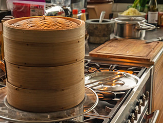 Close up shot of a Japanese cooking Steamer. The steamer stands on top of boiling water cooking food in a rustic beautiful kitchen. Steam can be seen coming form the top of the steamer.