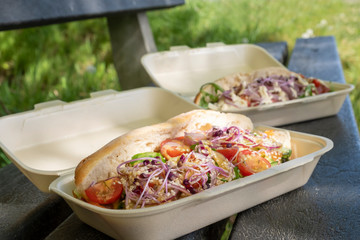 Lunch in nature, paper bag with sandwiches, coffee tea and orange juice are in front of the bag on the picnic bench. Recycling and environmentally friendly product concept. Take away food