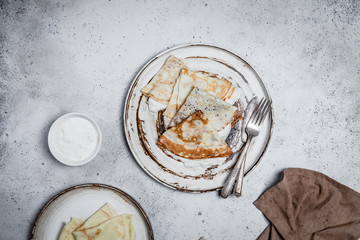 baked crepes in plates with forks and textile on shabby grey background, top view