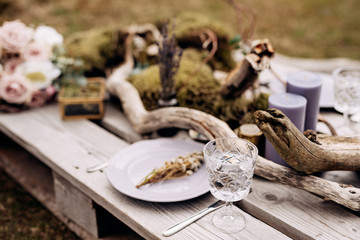 Close-up of a wedding dinner table. A table made of construction pallet decorated with driftwood and a car. The branches of the tree lie among plates and glasses. Wedding in Iceland