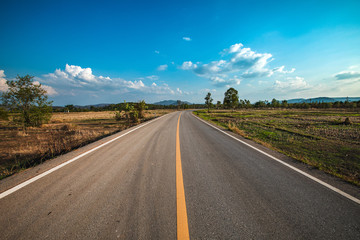 open road. Asphalt road through the green field and clouds on blue sky in summer day. 
