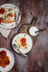 pancakes with blood oranges, nuts and cream in plates on wooden background, top view, traditional breakfast concept