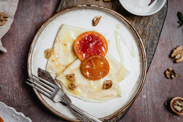 pancakes with blood oranges, nuts and cream in plates on wooden background, top view, traditional breakfast concept