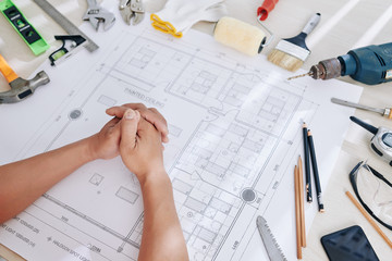 Construction engineer sitting at desk with working tools and blueprint of house