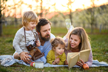 Family and small children with camera and book outdoors in spring nature, resting.
