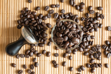 A cup of coffee beans and a tamper on bamboo mat