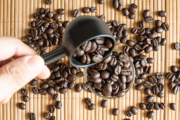 A cup of coffee beans and a measuring spoon on bamboo mat